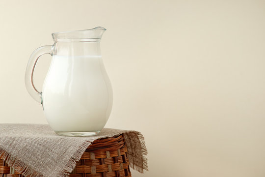 A jug of milk on a beige background. A jug of milk on a wicker basket in a rustic style. Milk on burlap in the village.