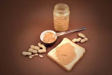 Glass of peanut butter stock images. Jar of peanut butter on brown background. Toast with peanut butter. Breakfast still life. American delicacy