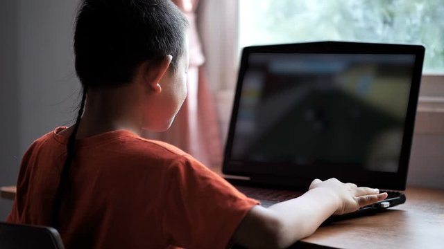 Asian boy 7 years old using laptop playing the game with Internet Information at home. Concept of technology in everyday life...