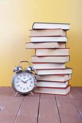 Science and education -  alarm clock and high group of red books on the wooden table