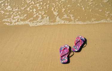 Pair of vibrant colored flip-flops or sandals on golden sand beach with the wave swash 