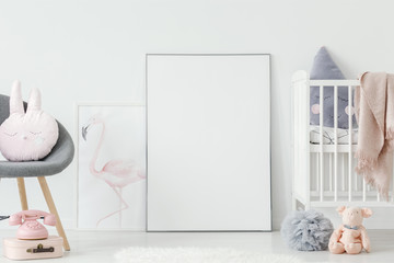 Flamingo poster standing on the floor behind empty mockup poster in white baby room interior with...