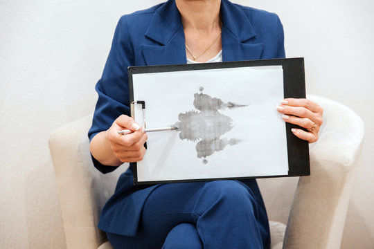Woman is sitting and holding a picture. It is hand drawing. It is attached to the tablet. Woman is pointing on picture with pen.