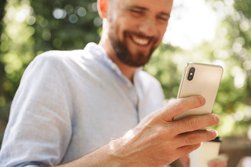 Happy young bearded man outdoors using mobile phone.