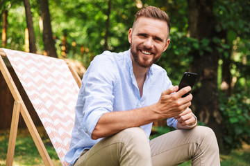 Happy young bearded man outdoors using mobile phone.