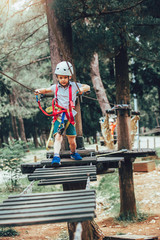 Obraz na płótnie Canvas Little boy climbing in adventure activity park with helmet and safety equipment