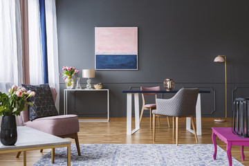 Pink and navy blue painting in grey living room interior with flowers and armchair. Real photo