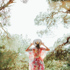 A hippie girl in a beautiful flying dress, hat and round glasses in a pine forest among the...