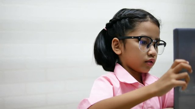 Little girl wear glasses is playing game on teblet