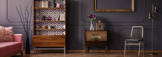 Fotobehang Gold chair standing in dark grey room interior with two vintage wooden cupboards with decor, books and fresh tulips © Photographee.eu