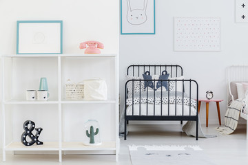 Kid's bedroom interior with a view of one whole bed and a part of the other. Shelves with...
