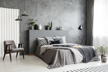Modern grey bedroom interior with big bed with pillows and linen. Comfortable armchair next to the...