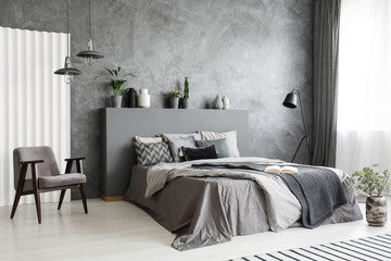 Modern grey bedroom interior with big bed with pillows and linen. Comfortable armchair next to the bed. Real photo.