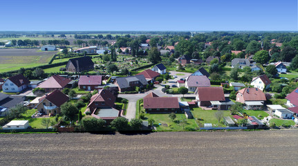 Fototapeta na wymiar Aerial view of a new housing estate with detached houses and gardens. At the edge of a village with a field in the foreground, near a cemetery