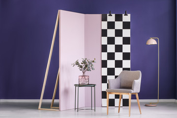 Partition wall with checkered pattern set in a purple room with an armchair, table and plant in...