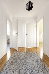 Real photo of a wide corridor with gray rug on the wooden floor and white door to other rooms