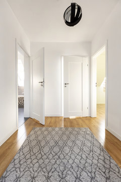 Real Photo Of A Wide Corridor With Gray Rug On The Wooden Floor And White Door To Other Rooms