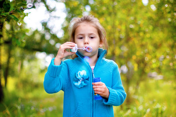 little girl with a ponytail in a blue sweatshirt blows bubbles