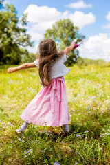 female child in a dress running on the grass in the summer and is happy