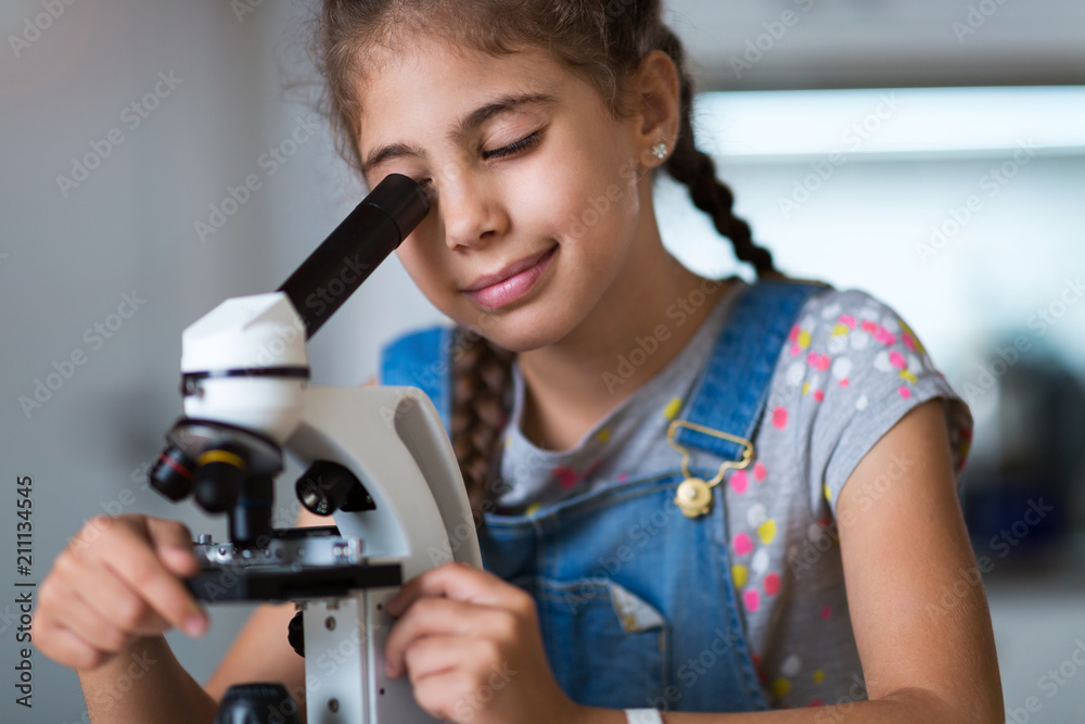 Wall mural young girl looking through microscope