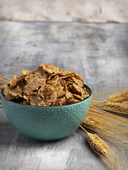 Wheat flakes in a ceramic bowl with ears of wheat on gray background. Horizontal. Copy space