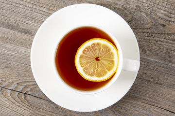 Tea with lemon in a white mug on a wooden table. Top view.