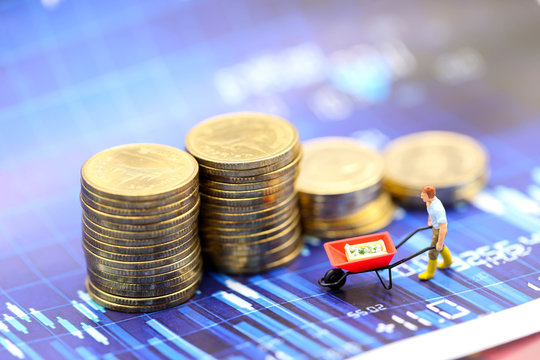 Miniature people : worker pulling stack coins with graph chart financial analysis review document.