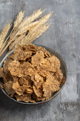 Wheat flakes in a ceramic bowl with ears of wheat on gray background. Horizontal. Copy space