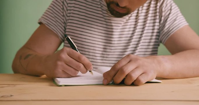 Young man against green screen writing in notebook