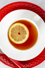 Tea with lemon in a white mug on a red plate. On a wooden table. Tea spoon. Top view.