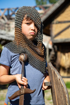 A young boy disguised as an unblemished knight with a sword, shield and basinet. 