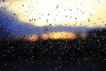Rain outside window on sunset background. Water drops on glass during raining