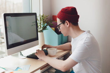 Young guy sitting and working at the computer - 211137543