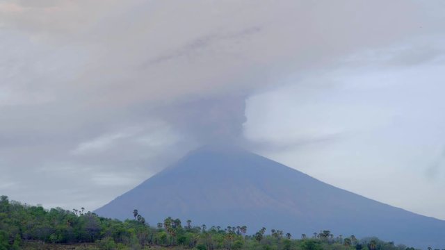 Dawn to day time lapse of Agung volcano erupting with ash plume rising from crater on the peak