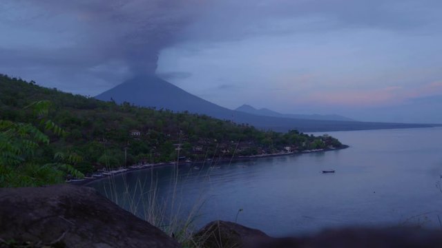Dawn to day time lapse of Agung volcano erupting with ash plume and Amed beach in Bali, Indonesia