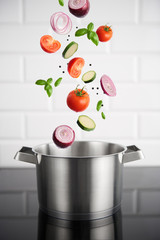 Healthy eating. Stainless steel pot with vegetables on the induction stove with white metro tiles in the background. High resolution product.