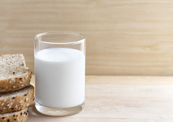 A glass of milk and bread placed on the wood table.