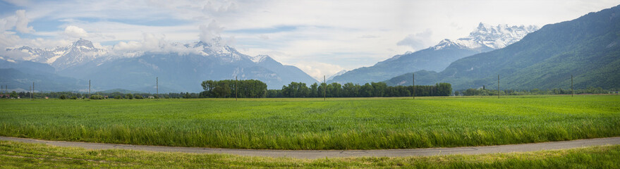 Naklejka premium This superwide ground level panorama exemplifies the true beauty of the beautiful Swiss Valais Valley. The Franco-Swiss Alps form a wonderful backdrop & so does the cycling track in the foreground.