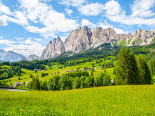 Fototapeta na wymiar Rocky ridge of Pomagagnon Mountain above Cortina d'Ampezzo with green meadows and blue sky with white summer clouds, Dolomites,, Italy.