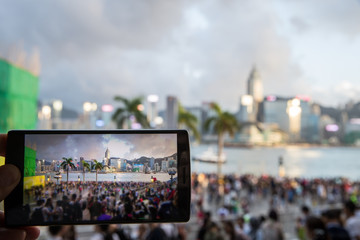 Man using his Mobile Phone to take photo of the crowed at seafront, twilight background