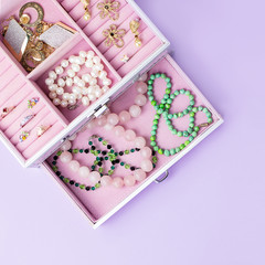 Open jewelry box with neclaces, earrings and rings on pastel background. Top view