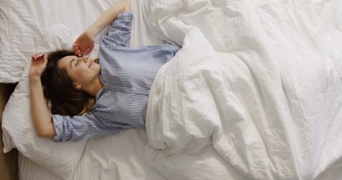 Attractive young Caucasian woman waking up in the early morning, then lying and stretching. At home. Indoor.