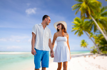travel, tourism and summer vacation concept - happy couple on vacation wearing sunglasses and walking holding hands over tropical beach background in french polynesia
