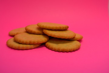 On the pink paper background, fresh salty biscuits are located and placed, crispy delicious round crackers with dots