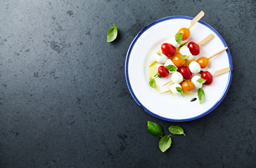 Cherry Tomato and Mozzarella Skewers with basil leaves and olive oil on a plate. Summer snack. Flat lay. Healthy food