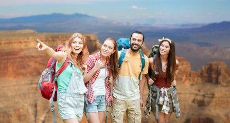 travel, tourism, hike and adventure concept - group of smiling friends with backpacks pointing...