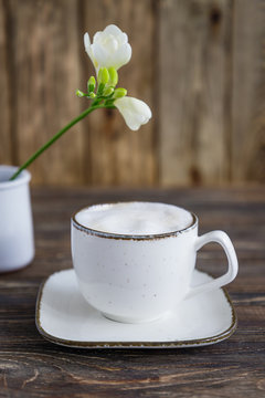White cup of coffee cappuccino and white freesia flower on a wooden background. Free space, vertical photo