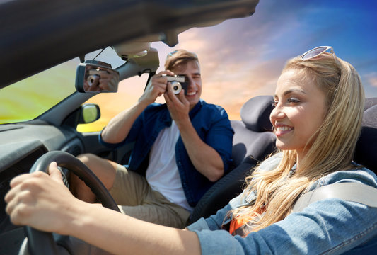leisure, road trip, travel and people concept - happy couple driving in convertible car and taking picture by film camera over sky background