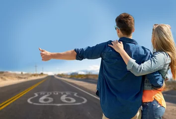 Fototapeten road trip, hitchhike, travel and gesture concept - happy couple hitchhiking over us route 66 background © Syda Productions