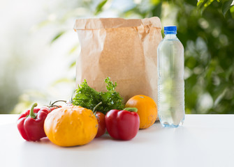 food, diet and healthy eating concept - paper bag with fresh vegetables and water bottle on table over green natural background